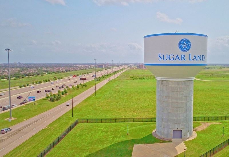 Sugar Land water tower with blue top overlooking green fields and a highway in the distance