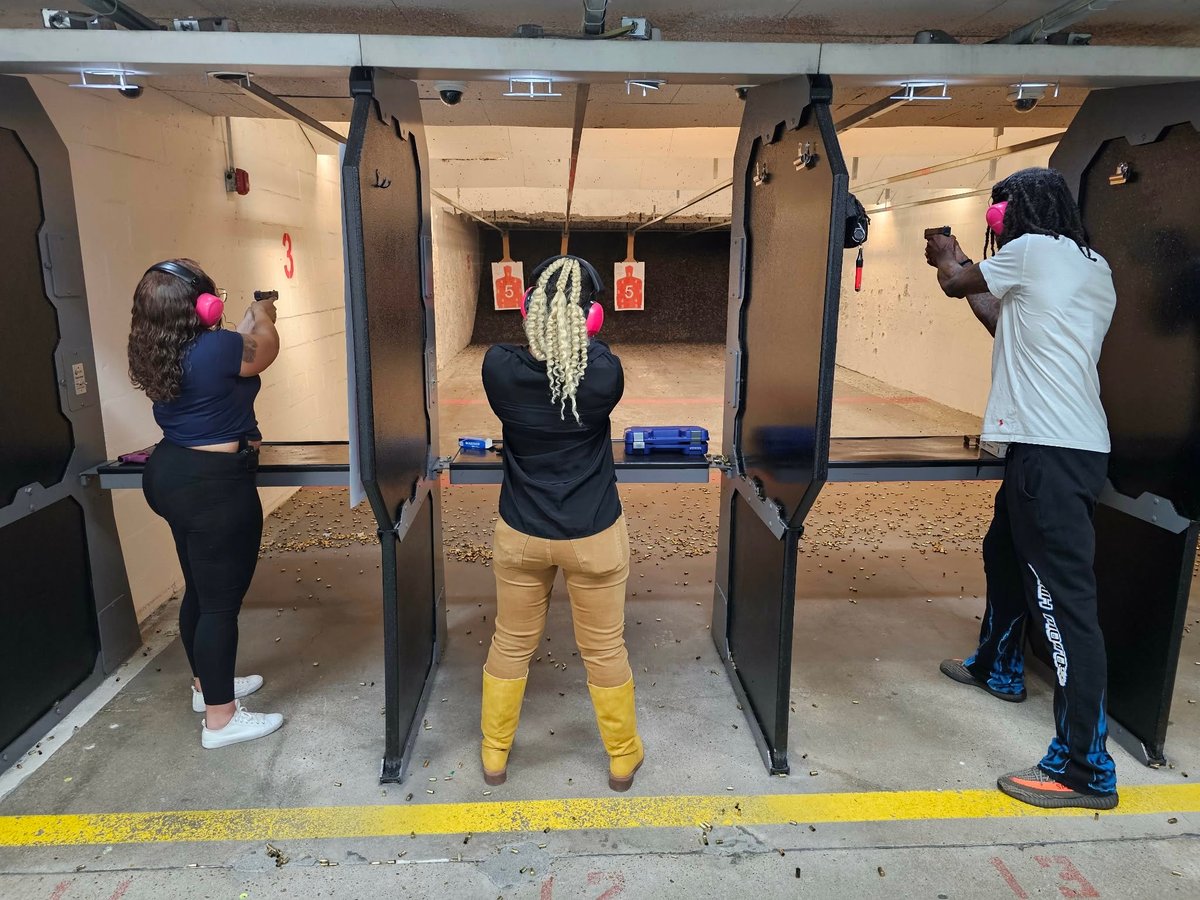 Three people practicing at individual shooting ranges with targets and firearms in an indoor shooting facility