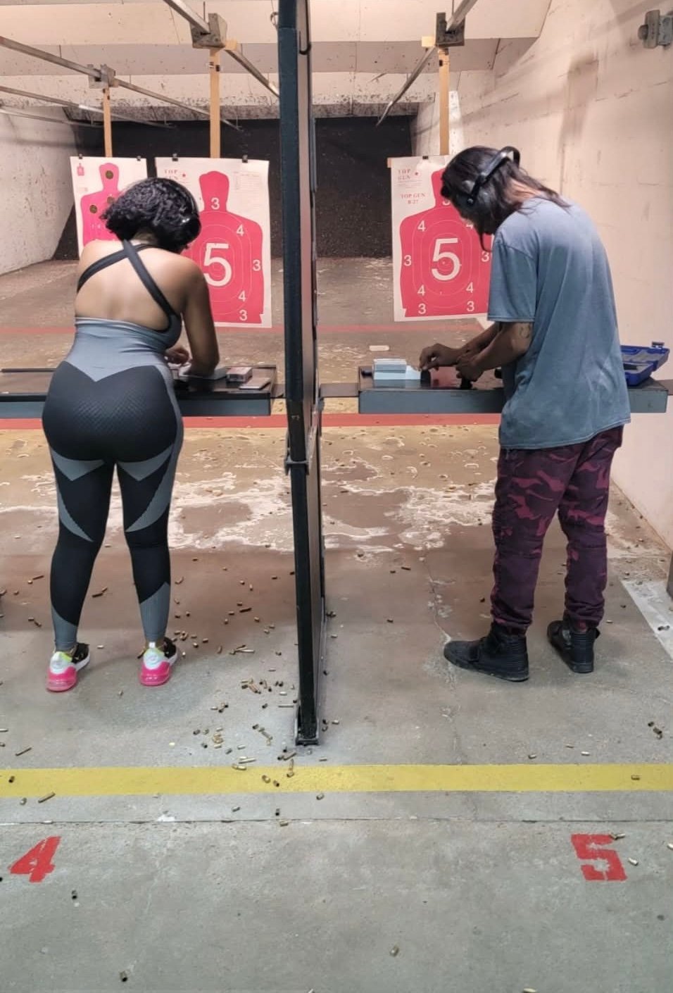 Two people at a shooting range practicing with firearms at pink and white numbered targets