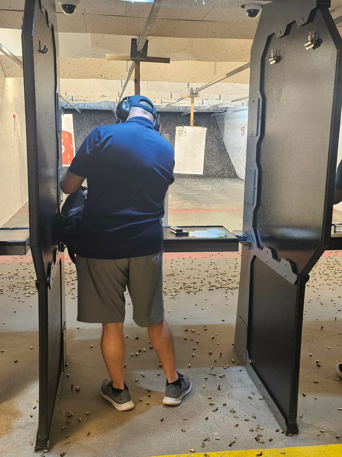 Person in blue jacket shooting at target range between black barriers at indoor firing range