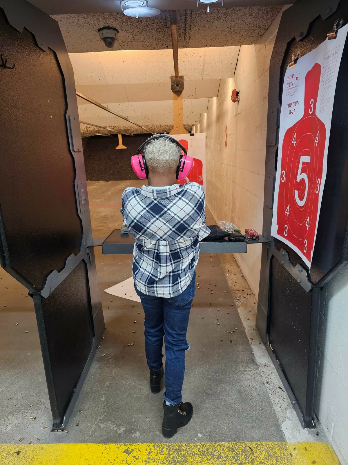 Person wearing hearing protection at an indoor shooting range with red target visible on the right