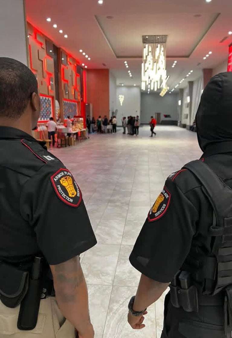 Two police officers viewed from behind monitoring a modern public venue with red architectural elements and scattered visitors