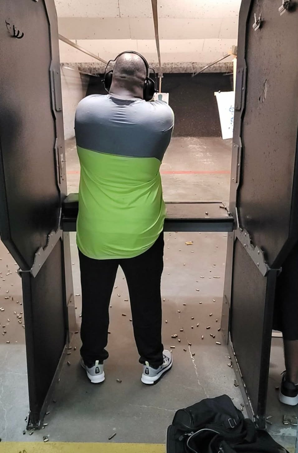 Person wearing headphones and neon green vest shooting at indoor shooting range target with concrete walls
