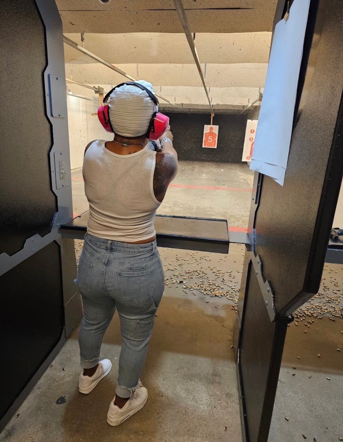 Person wearing headphones and protective gear standing in an indoor shooting range aiming at targets downrange