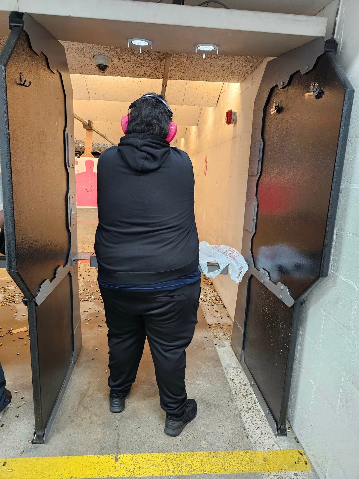 Person in black jacket and pink headphones standing inside a utility closet or storage space with corrugated metal walls