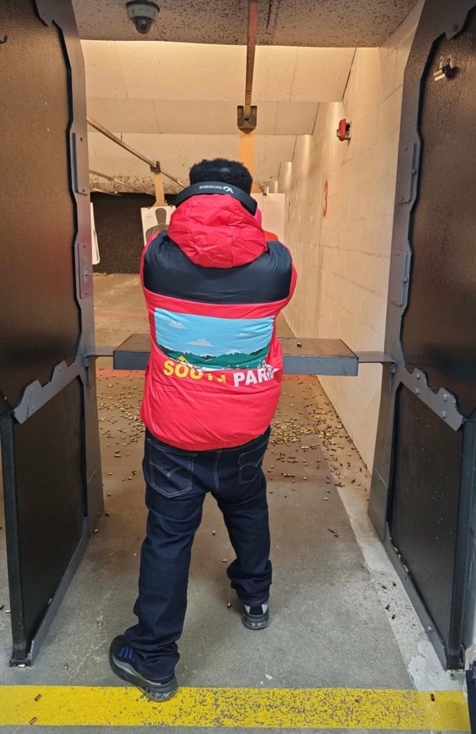 Person wearing red and black South Park jacket walking through narrow corridor viewed from behind
