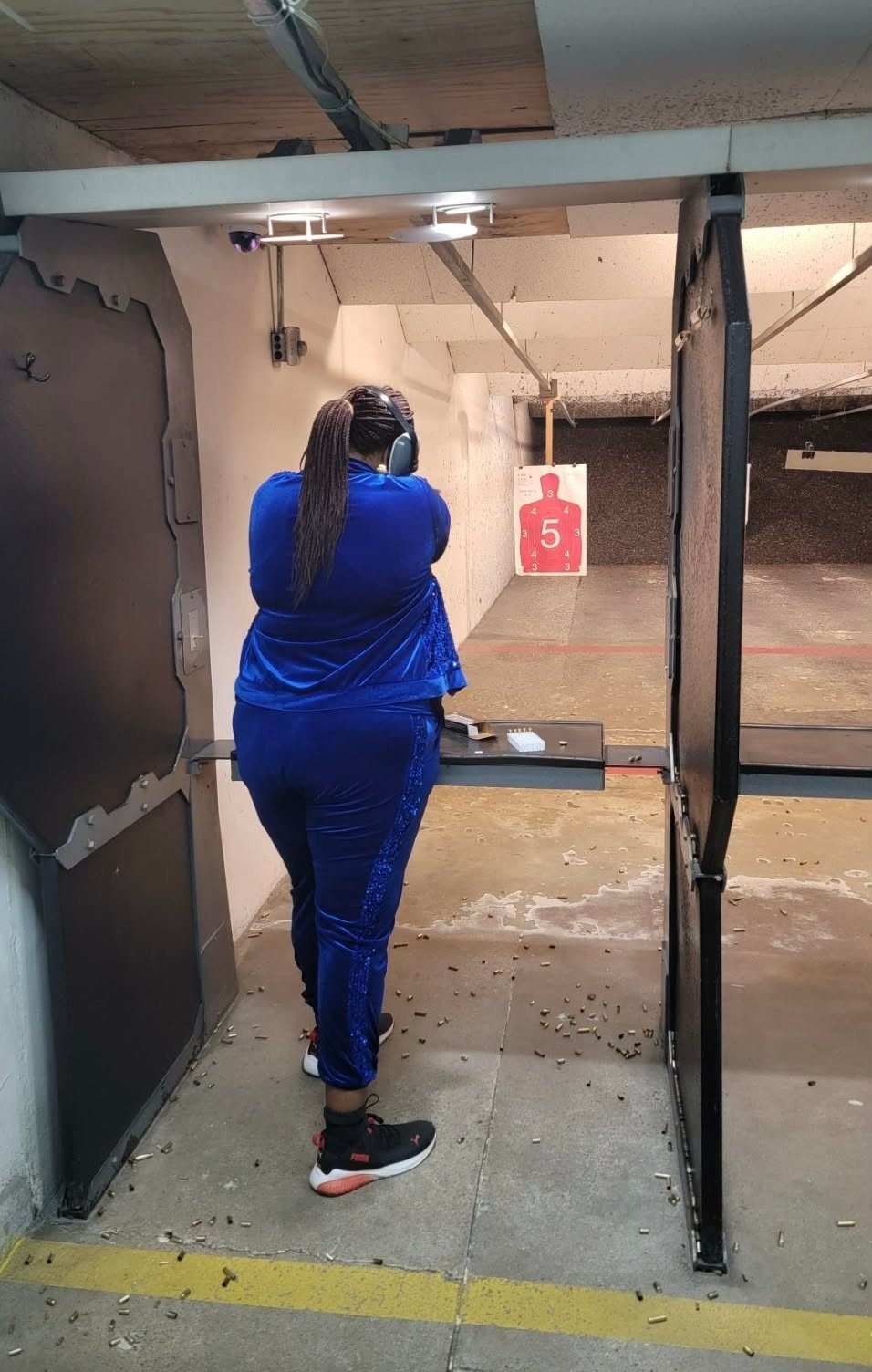 Person in blue outfit at an indoor shooting range aiming at a red target marked with number 5