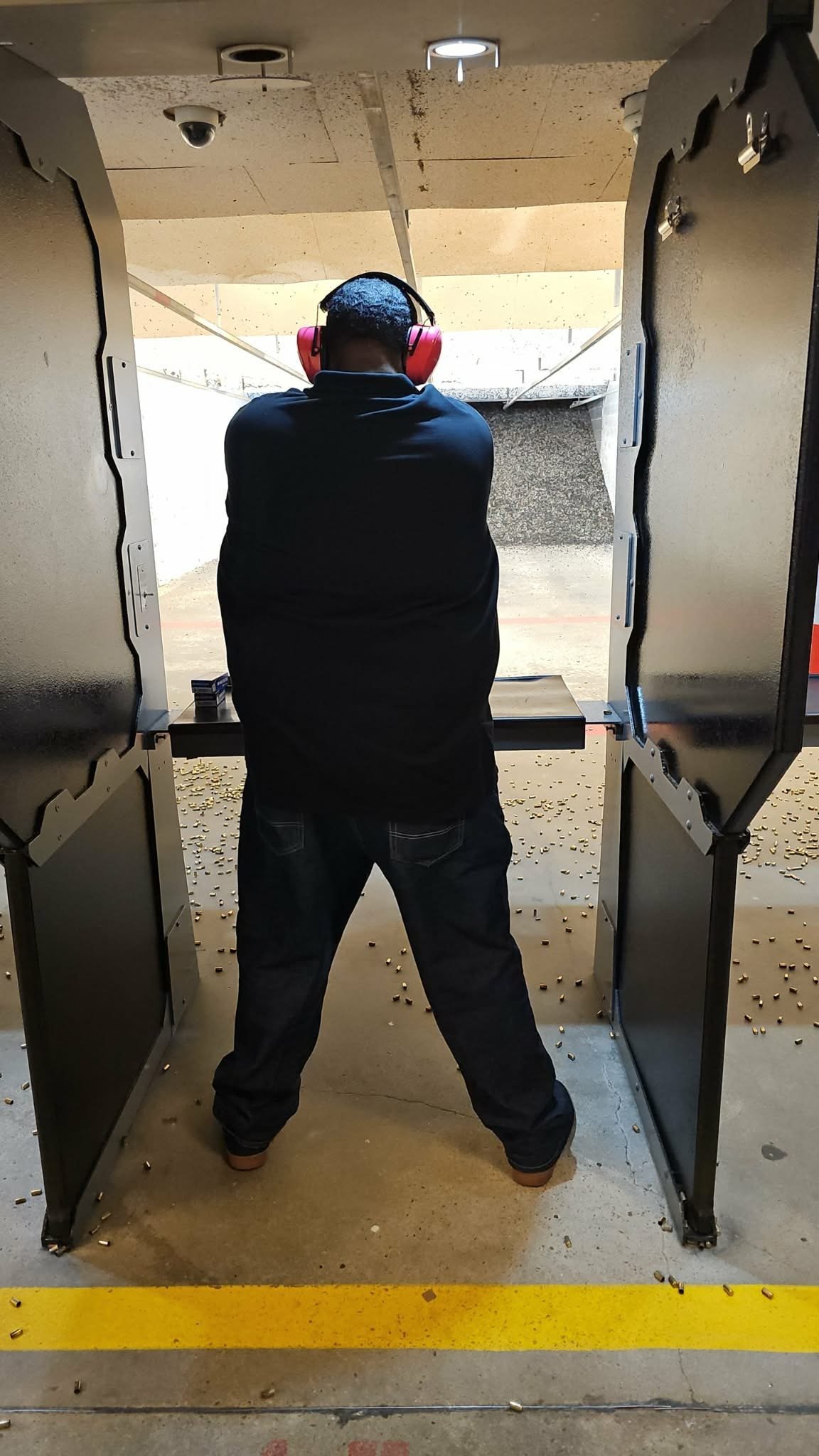 Person wearing hearing protection in a shooting range booth standing at firing line facing downrange