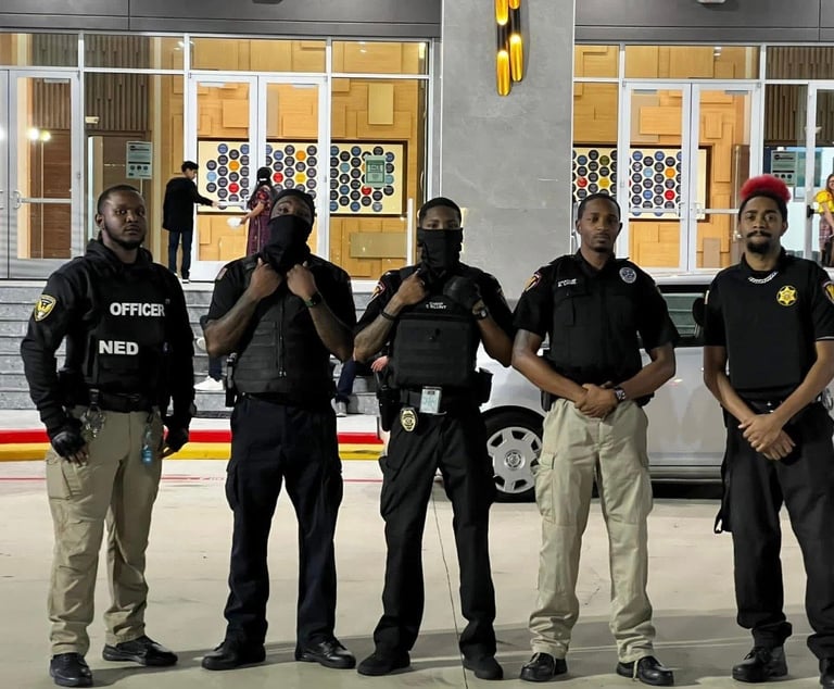 Five law enforcement officers standing in a line inside a facility with glass doors and windows behind them