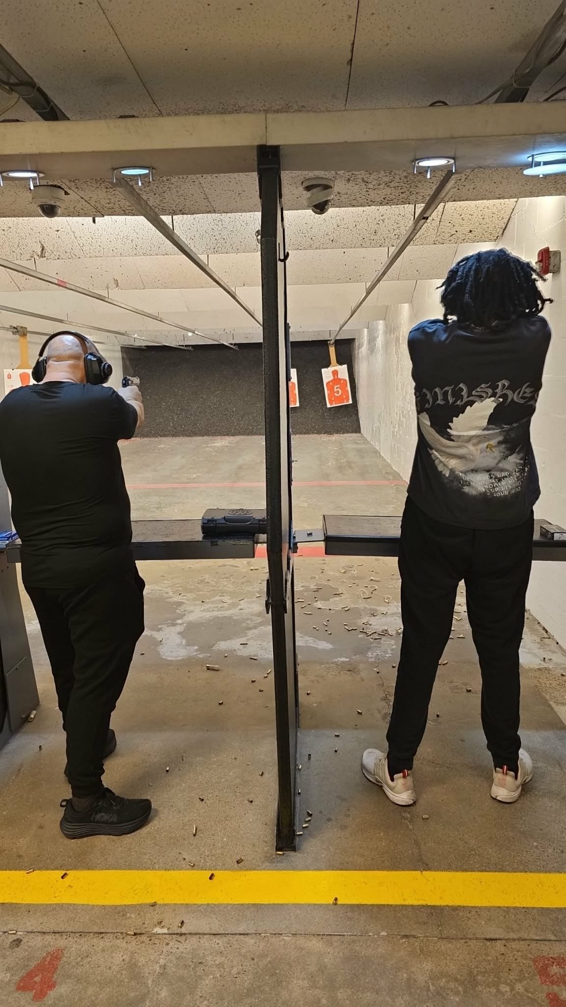 Two people wearing hearing protection at an indoor shooting range, aiming at targets downrange
