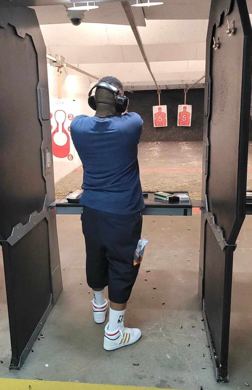 Person in blue shirt and headphones aiming at targets in an indoor shooting range booth