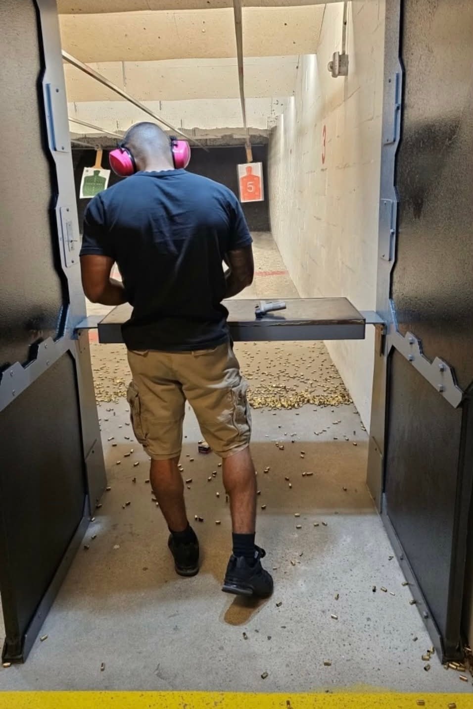 Person wearing pink earmuffs and dark shirt at an indoor shooting range aiming at targets