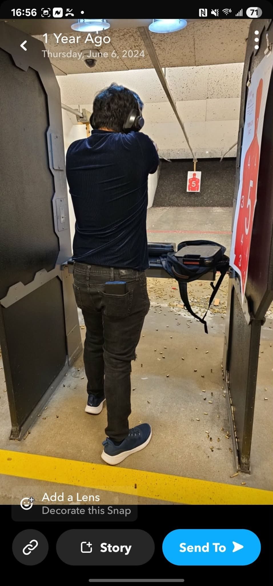 Person wearing headphones at indoor shooting range, aiming at target downrange with gun on table