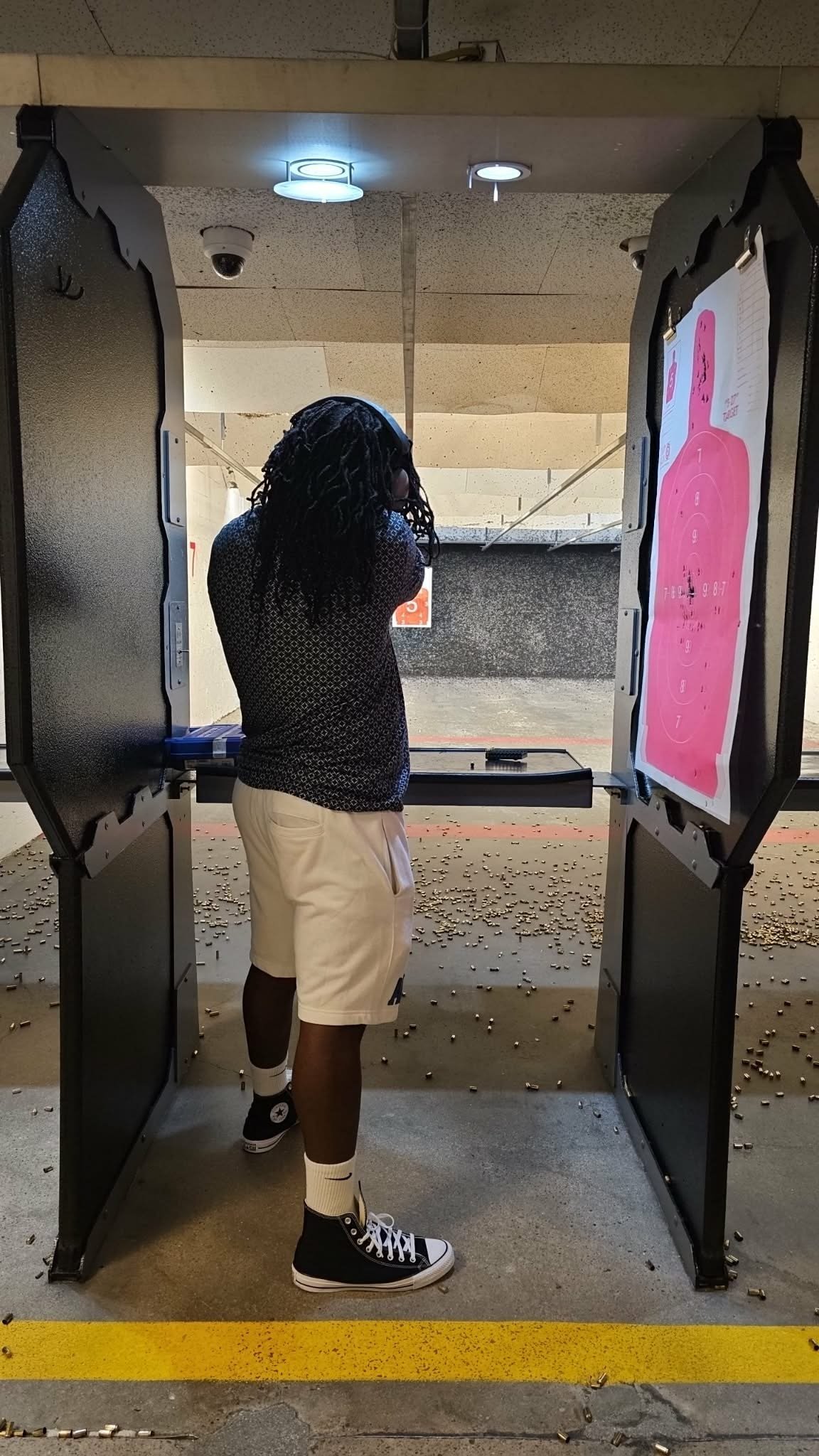 Person in shooting stance at indoor gun range, aiming at pink target on wall with firearm