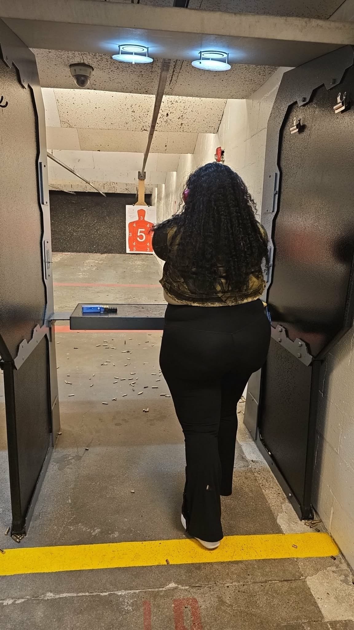 Person aiming at orange target number 5 at indoor shooting range with concrete walls and overhead lighting
