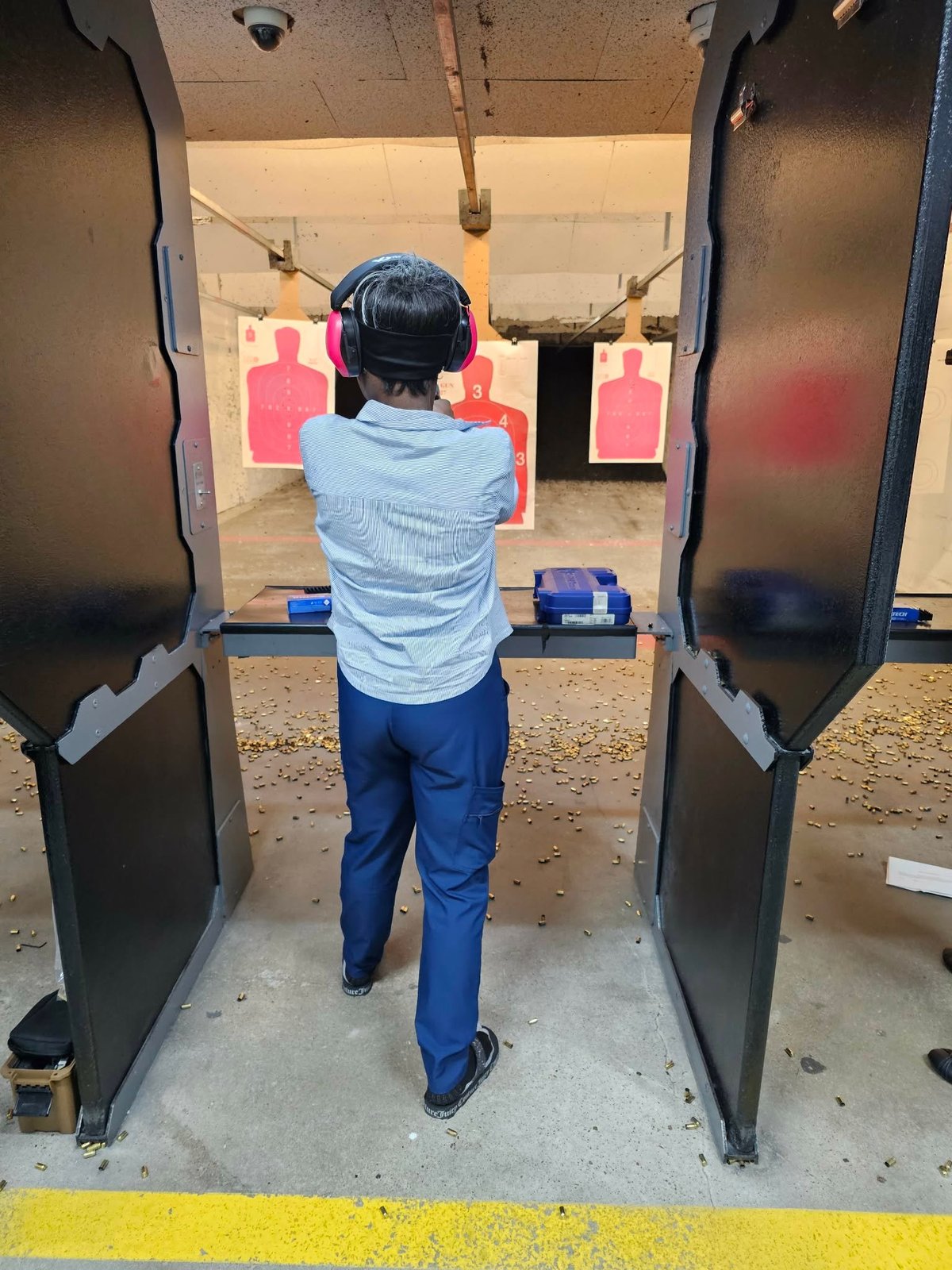 Person at shooting range in protective gear aiming at pink paper targets downrange
