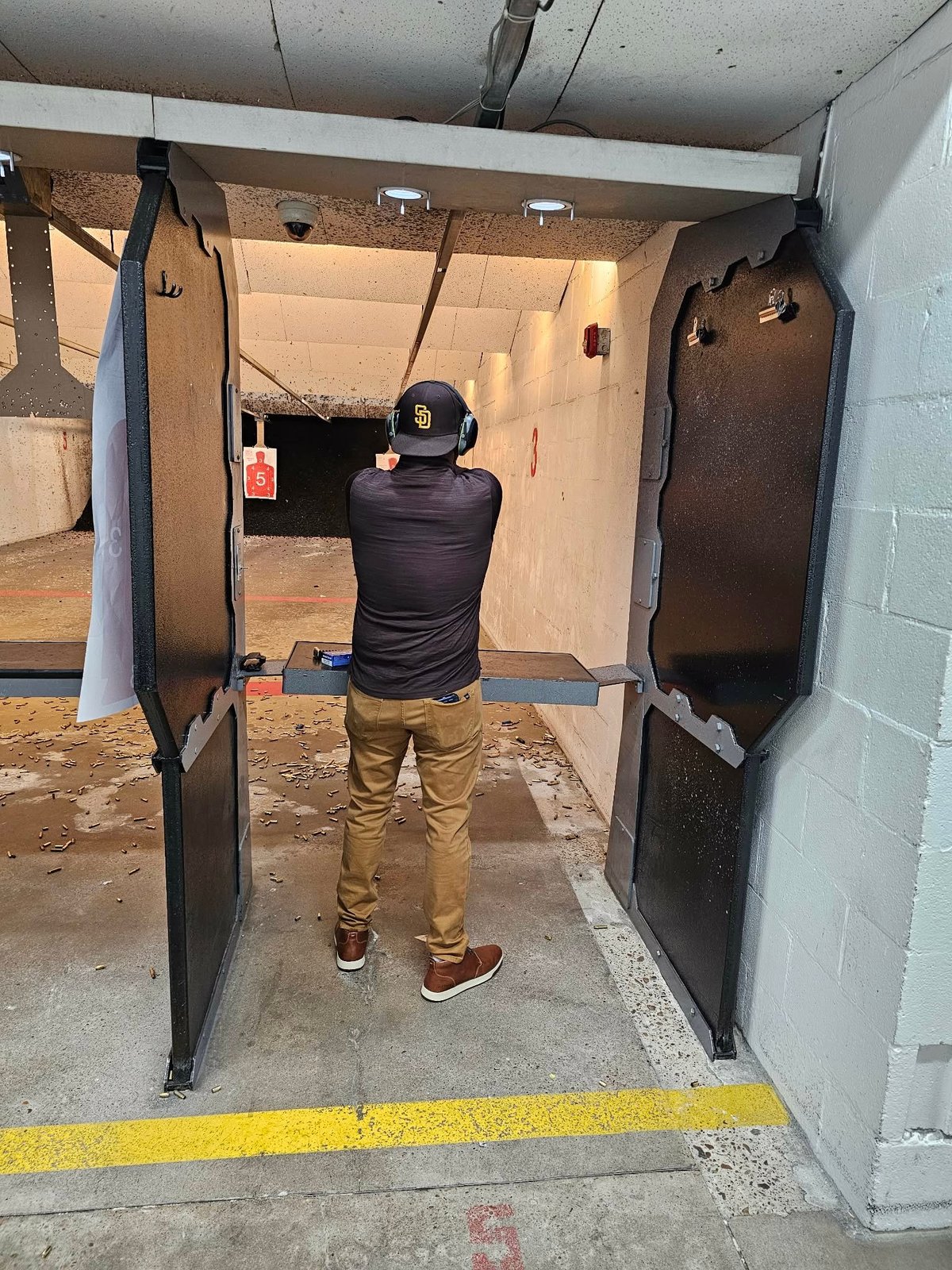 Person in shooting stance at indoor gun range, aiming at targets in a narrow shooting bay