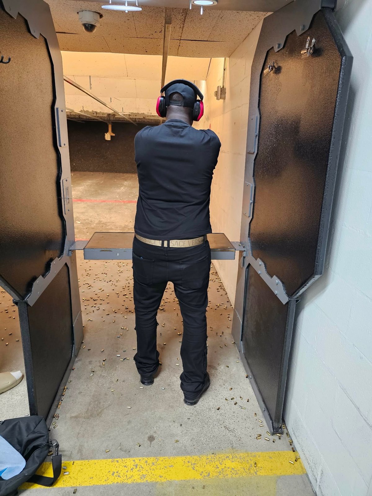 Person in black clothing and red headphones at indoor shooting range preparing to shoot at targets