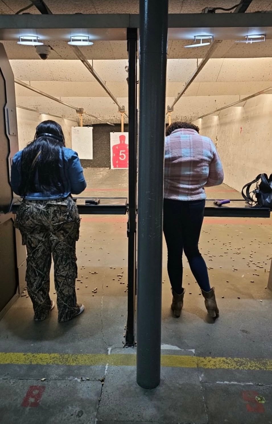 Two people aiming firearms at targets in an indoor shooting range with target markers visible