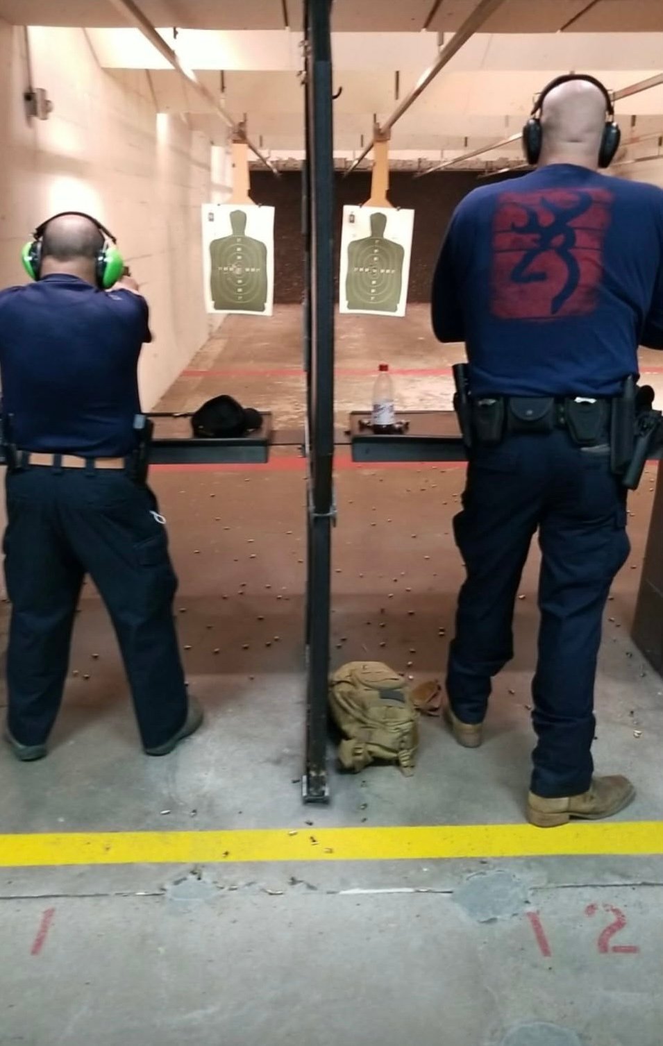 Two police officers at an indoor shooting range facing target practice silhouettes while wearing headphones